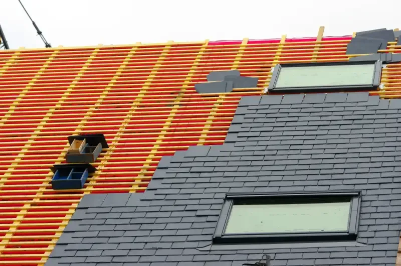 Toiture en cours de couverture avec ardoises et fenêtres de toit Velux, sur une charpente visible.