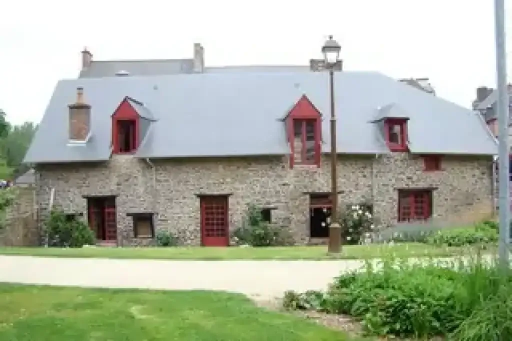 Maison en pierre dotée d'une toiture en ardoises grises et de lucarnes rouges, dans un environnement verdoyant.