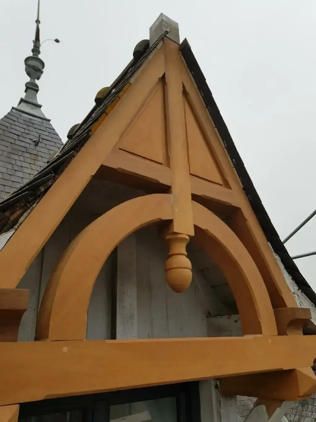 Vue rapprochée d'un pignon en charpente bois ouvragée, associé à une toiture en ardoises d'un bâtiment ancien.