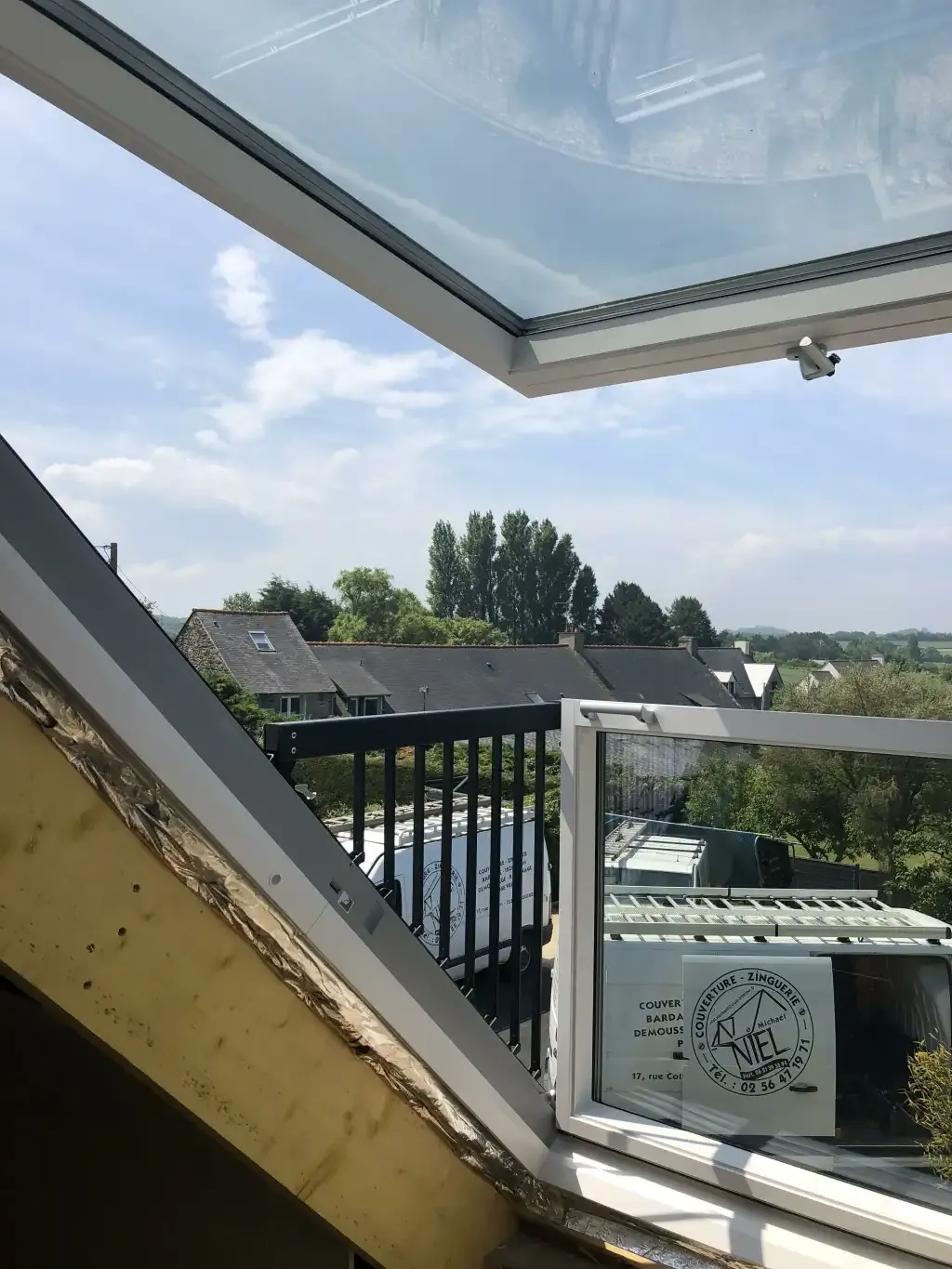 Fenêtre de toit Velux ouverte sur un paysage résidentiel, avec l'isolation de la toiture visible