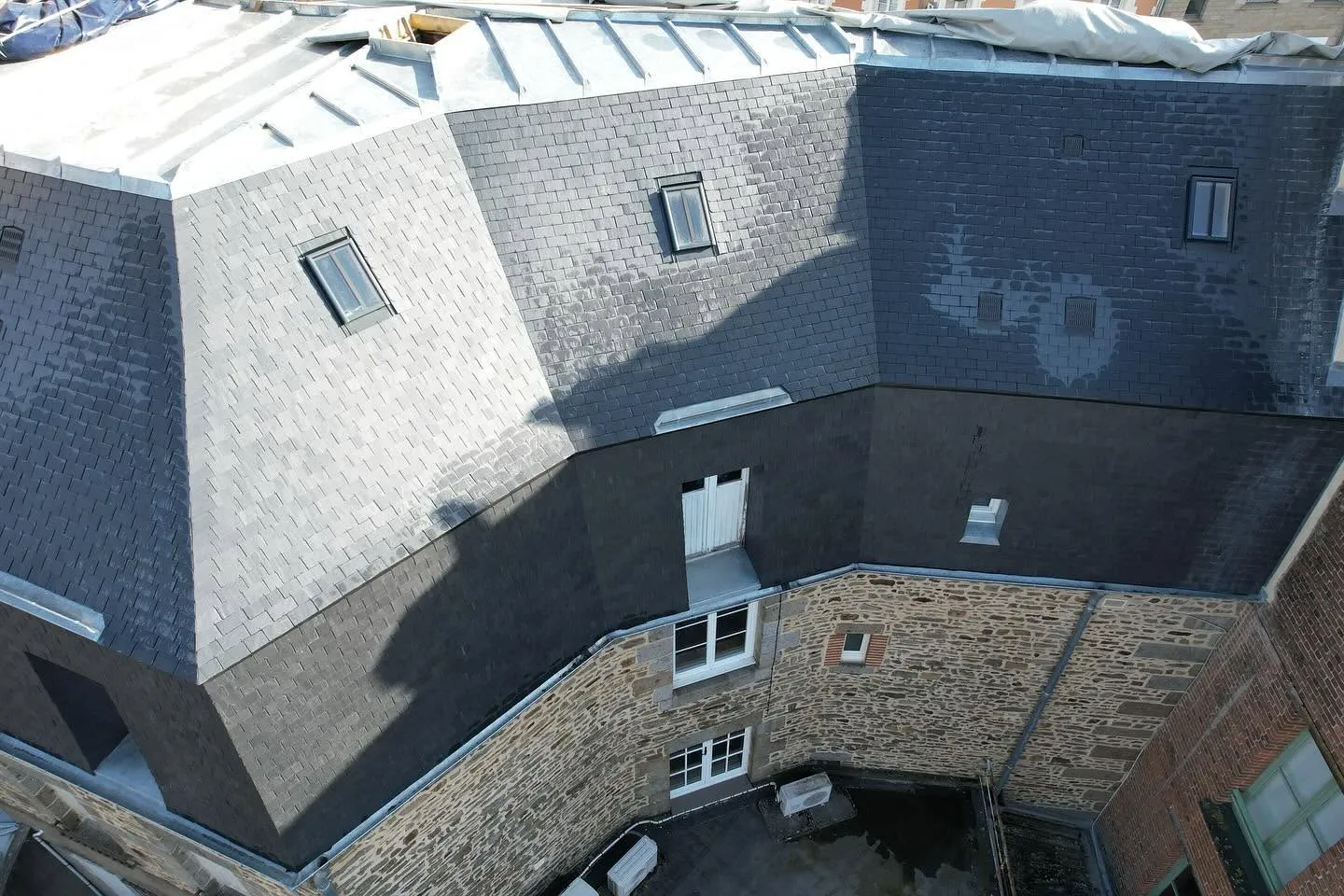 Vue aérienne d'un grand toit en ardoise avec fenêtres de toit au-dessus d'une façade en pierre